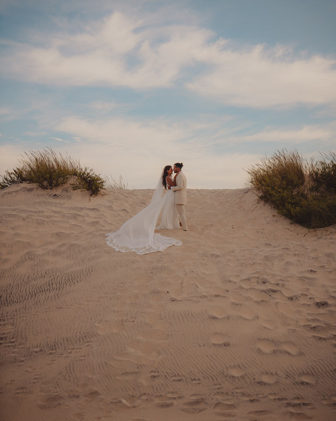 Los novios cruzando las dunas blancas de Huelva bajo un cielo enorme de tarde, fotografía editorial de boda de Gorka Di Capitan