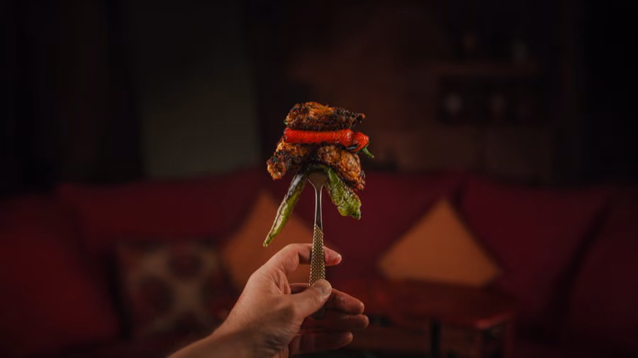 Hand raising a fork loaded with charcoal grilled meat and pepper in the red dining room at Beirut Restaurant