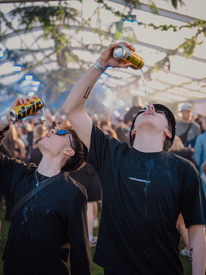 Festival-goers pouring DRIP water cans at Terminal V, one wearing a Terminal V t-shirt