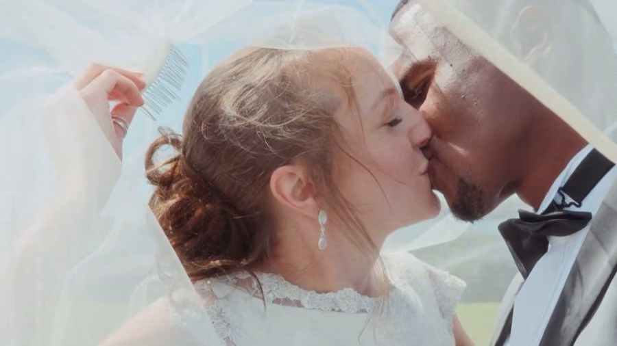 Emma and Sibo kissing under her flowing veil against a blue Highland sky on their wedding day