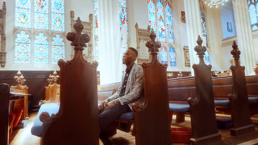 Kishaolin sentado en los bancos tallados de una catedral escocesa en el videoclip de Lord Almighty
