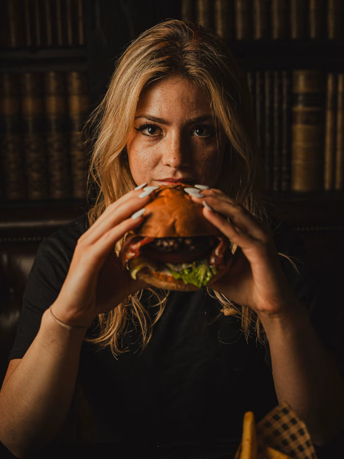 Blonde guest biting into a burger at The Piper's Rest, Edinburgh