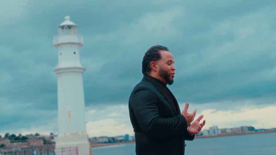 Robert Rufino singing in a black suit by the Newhaven lighthouse under a stormy teal sky