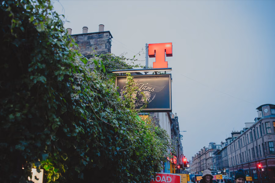 The Twa Tams pub sign beneath the red Tennent's T, wrapped in ivy on the Perth street