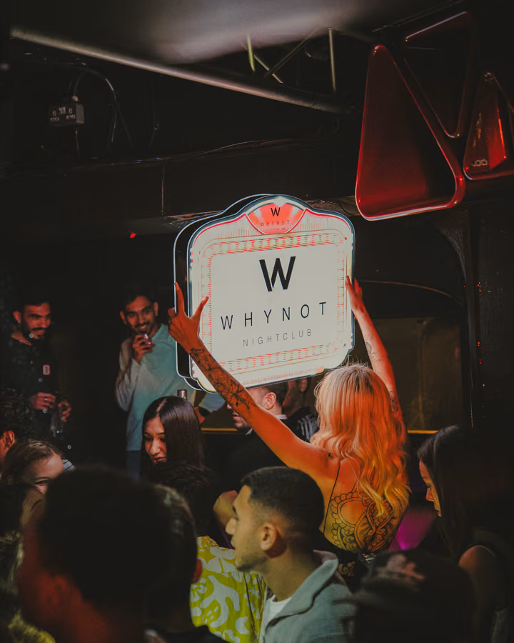 Guest holding up the illuminated Why Not Nightclub sign above the crowd